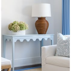 a white couch sitting next to a table with a lamp on top of it and a vase filled with flowers