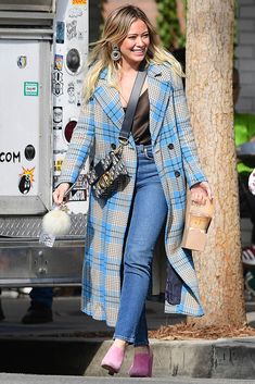 a woman in plaid coat and jeans walking down the street