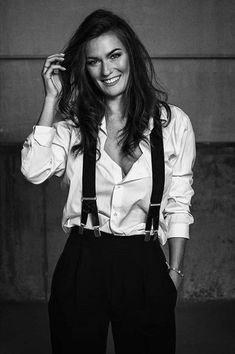 a black and white photo of a woman with long hair wearing suspenders, smiling