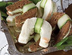 cucumber sandwiches are arranged on top of leafy greens in a silver tray