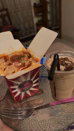 a person holding a fork next to a box of food on a tray with a drink in it