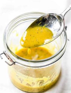 a spoon is full of yellow sauce in a jar