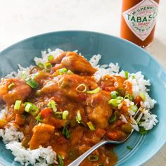 a blue plate topped with rice and meat covered in sauce next to a bottle of tabasco