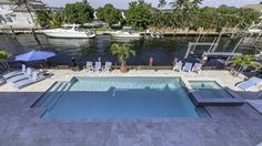 an outdoor swimming pool with lounge chairs and umbrellas next to the water, surrounded by palm trees