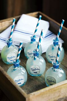 six bottles with blue and white striped drinking straws in them on a wooden tray