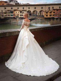 a woman in a wedding dress leaning against a wall with her back to the camera