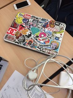 a laptop computer sitting on top of a wooden desk next to a pile of stickers