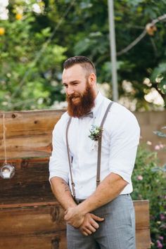 a man with a beard and suspenders standing in front of a wooden box filled with flowers