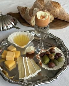 an assortment of cheeses, olives and bread on a silver tray