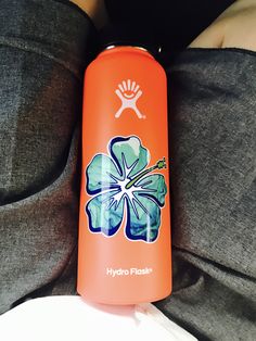 an orange hydro flask with a flower painted on the side sitting on someone's stomach