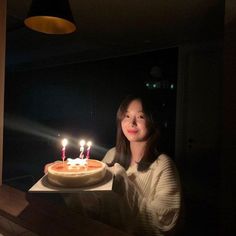 a woman sitting in front of a cake with lit candles