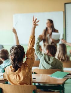 a group of children sitting at desks with their hands in the air