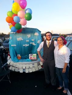 a man and woman standing next to a car with balloons on the back of it