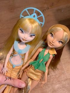 two dolls sitting next to each other on top of a wooden floor in front of a person's hand