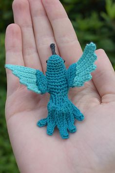 a hand holding a tiny crocheted bird in it's palm