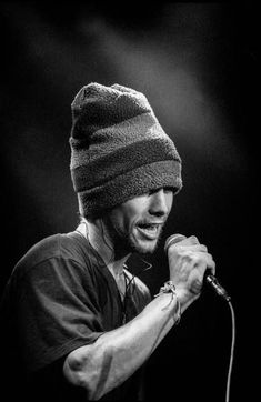 a black and white photo of a man with a hat on singing into a microphone