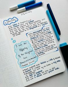 an open notebook with writing on it next to two blue pens and a black marker