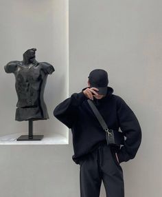 a man standing in front of a statue and holding his head to his face with one hand