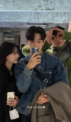 two people are looking at their cell phones while one person is taking a selfie