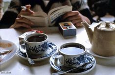 two cups and saucers on a white table with a person reading in the background