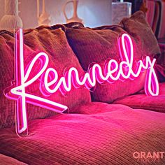 a pink neon sign sitting on top of a bed next to pillows and a lamp