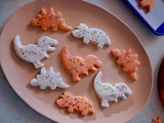 decorated cookies on a plate with sprinkles and frosting in the shape of dinosaurs