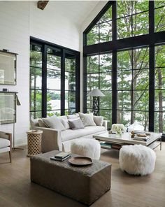 a living room filled with lots of windows next to a white couch and ottomans