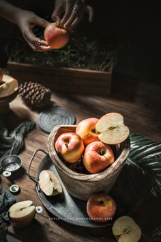 apples are in a wooden bowl on a black plate with pine cones and other decorations