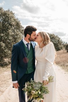 a bride and groom kissing on the side of a dirt road with trees in the background