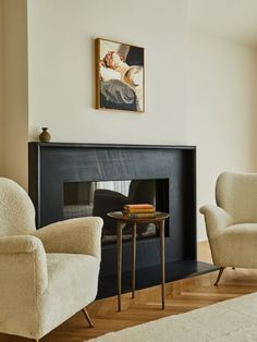 two chairs and a table in front of a fire place with a painting on the wall