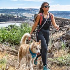 a woman is walking with her dog on a trail near some rocks and water in the background