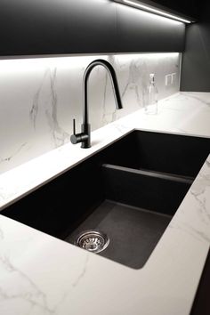 a kitchen sink with a black faucet and white marble counter top in front of it