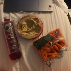 an open laptop computer sitting on top of a bed next to carrots and dip