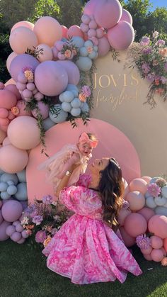 a woman in a pink dress standing next to a giant balloon arch with flowers on it