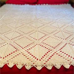 a white crocheted blanket on top of a bed with red sheets and pillows