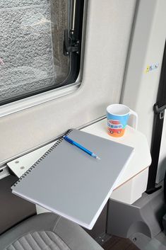 a notebook, pen and cup on a table in a vehicle