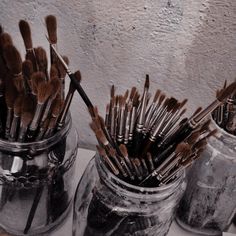 two jars filled with brushes sitting on top of a table