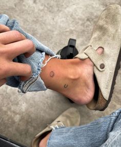 a person with a small tattoo on their left foot, sitting down and holding onto a pair of jeans