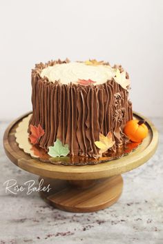 a chocolate cake with frosting and fall leaves on the top is sitting on a wooden stand