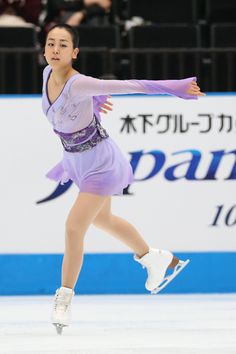 a woman skating on an ice rink wearing a purple dress and white shoes with her arms outstretched