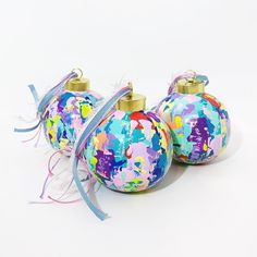 three ornaments with colorful paint splattered on them and ribbon tied around the top