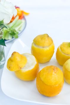 four lemons on a white plate with flowers in the background