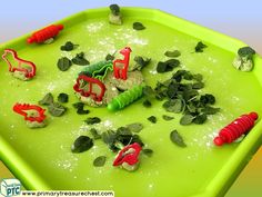 a green tray filled with different types of toy animals and plants on top of it