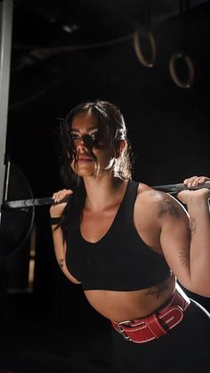 a woman is holding a barbell in her hands and looking at the camera while she squats