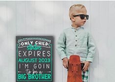 a little boy standing next to a sign with his skateboard in front of him