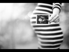 black and white photograph of pregnant woman in striped dress holding up an album with the image of a baby on it