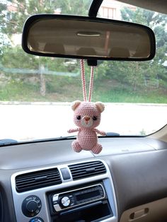 a pink teddy bear hanging from the dashboard of a car