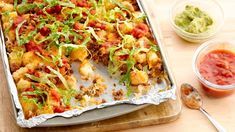 a pan filled with food next to two bowls of salsa and guacamole