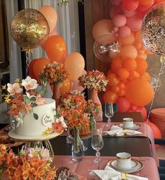 a table topped with a cake covered in lots of orange and pink flowers next to balloons