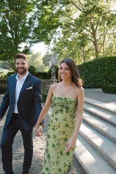 a man and woman holding hands while walking down some steps in front of trees with stairs leading up to them